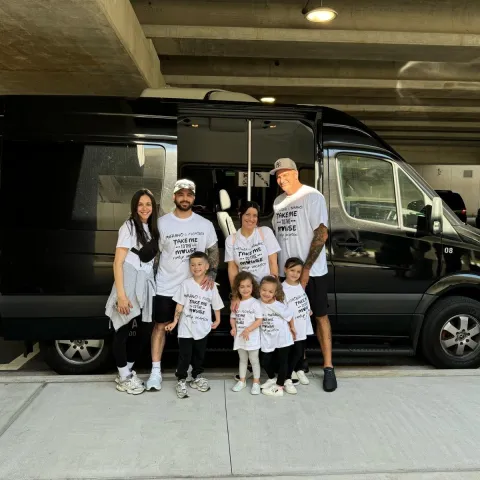 Family of seven wearing matching shirts posed by a black van in a parking structure.