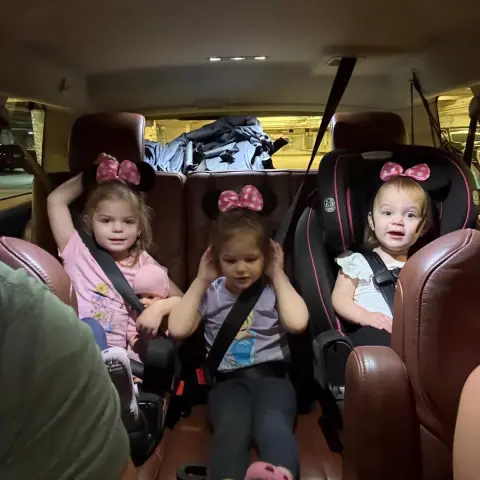 Three young children in a car, wearing Minnie Mouse ears.