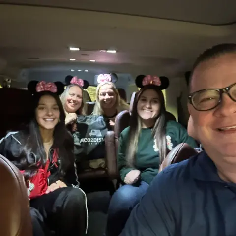 Group of people smiling in a car, some wearing Minnie Mouse ears.