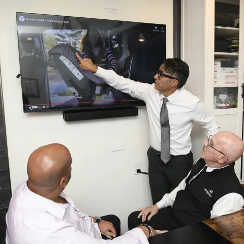 Three men engaged in a presentation displayed on a wall-mounted screen.